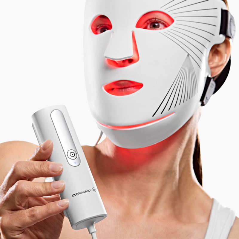 Woman wearing the CurrentBody Red Light LED Face Mask Series 2 and holding it's controller